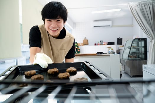 Cheerful small business owner putting a tray of chocolate chip cookies into the oven.
