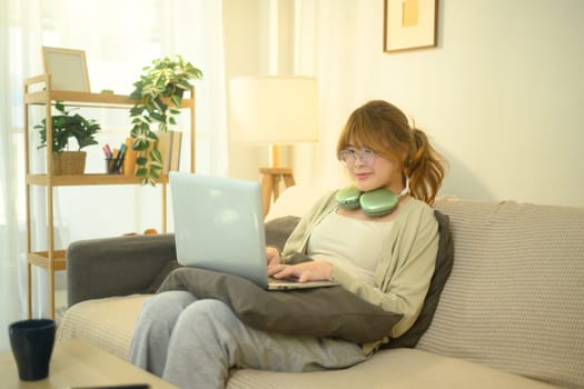 Young woman with glasses sitting on a sofa, working or online browsing in living room.