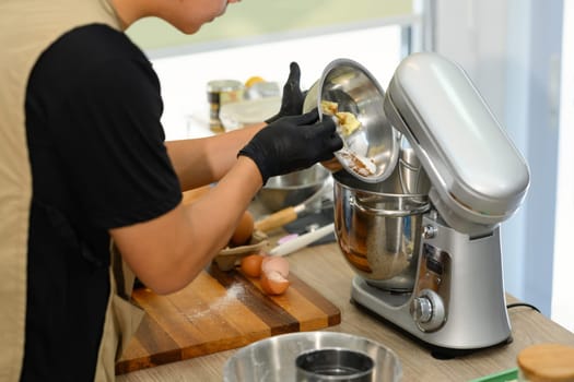 Young entrepreneur pouring ingredients into a a stand mixer, preparing cookie dough.