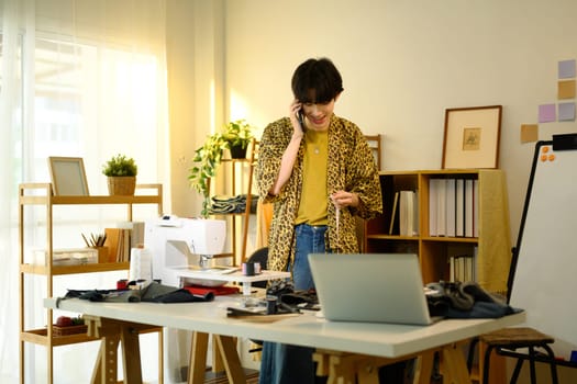 Smiling young designer having phone conversation in a creative fashion studio.