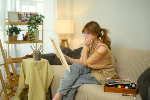 Thoughtful female artist holding a canvas while working on her latest piece in home studio.