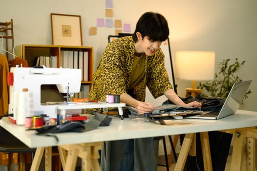 Young fashion designer working on denim design project and using laptop in a stylish workspace.