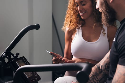 latin woman with curly hair in white top showing smartphone to man with tattoos in room, concept of technology of communication