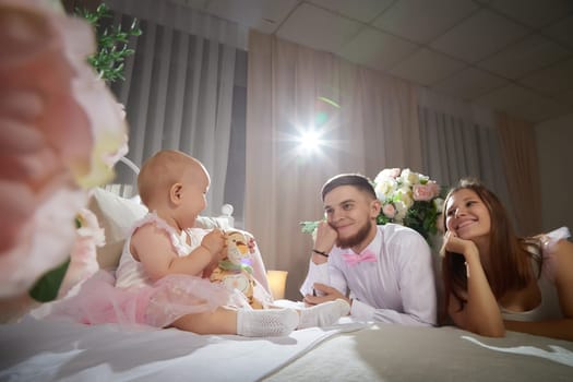 A couple enjoys a tender moment while their baby girl plays with a toy in a warm, inviting space filled with soft lighting on bed in beautiful room