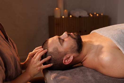 Relaxed man enjoying a head massage in a serene spa setting with calming candlelight ambiance and peaceful atmosphere.