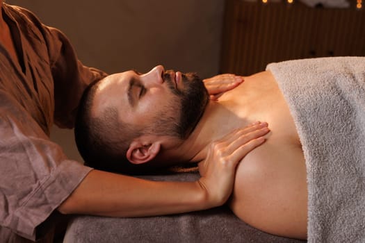 Man enjoying a soothing shoulder and neck massage in a tranquil spa, surrounded by soft lighting and a relaxing ambiance.