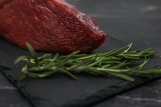 Close-up of red beef tenderloin on a black stone plank with a sprig of rosemary next to it on a black background. The concept of cooking, dietary menu, healthy and natural products. High quality photo