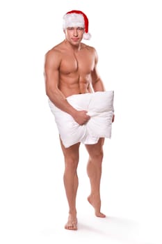 handsome sexy guy with naked torso wearing red Santa hat covering body with pillow standing on white background