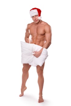 Full body of handsome sexy guy with naked torso wearing red Santa hat covering body with pillow standing on white background