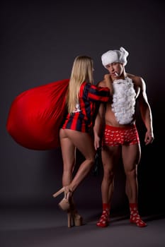 Side view of seductive blonde woman in striped garment and high heels enjoying time with sexy boyfriend in Santa Claus costume