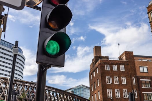 A green traffic light in an urban city setting, captured against a mix of modern and historic architecture under a blue sky