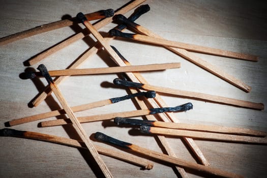 Elevated closeup view of burnt matches in spotlight on wooden background.