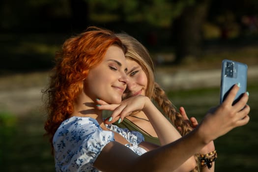 Two young women are happily posing for a cheerful selfie in a bright and sunny outdoor setting, capturing the moment