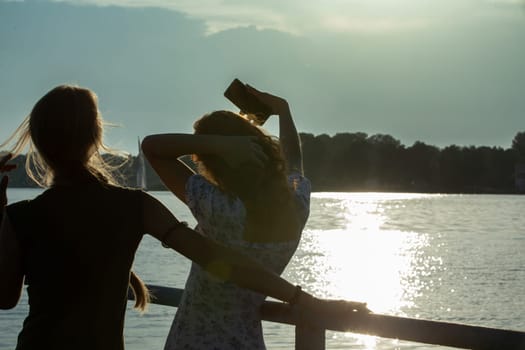 Two close friends are enjoying a beautiful sunset by the calm water, capturing a perfect moment of joy and serenity