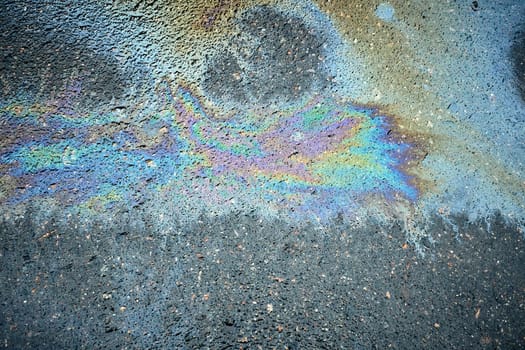 Up-close look at colorful oil patches, presenting a textured background filled with an array of tints on the road