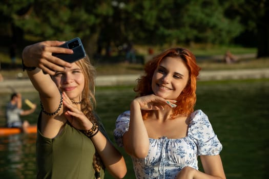 Two young women are enjoying a sunny day by the water, capturing joyful memories with a cheerful selfie