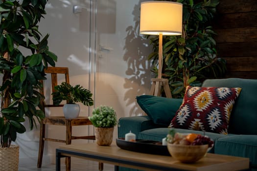 A stylish living room featuring greenery, a comfy sofa, and warm, inviting lighting throughout the area