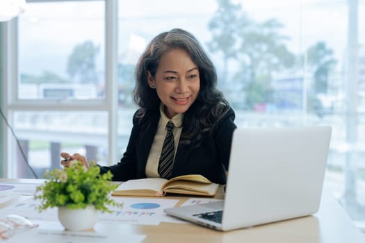 Smiling mature middle aged business woman using laptop working and sitting at desk.