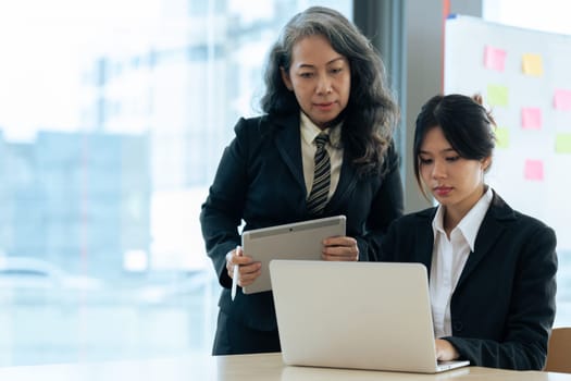 Two diverse financial assistant working on laptop while senior professional standing and giving investment advise.