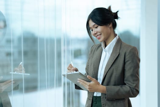 Businesswoman working on digital tablet while standing in front of windows.