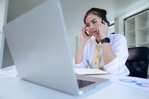 Tired business woman in stress works at a laptop while sitting at a table and holds her hand on her temples, migraine attack..