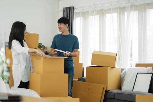 Asian young happy new married couple moving to their new house or real estate. An attractive romantic man and woman carry boxes parcel with happiness and love. Family moving house relocation concept.