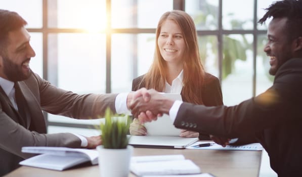 Sealing a deal. Business people shaking hands while sitting at the desk in office