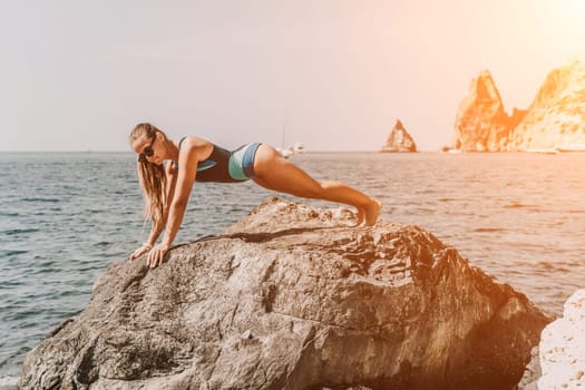 Yoga on the beach. A happy woman meditating in a yoga pose on the beach, surrounded by the ocean and rock mountains, promoting a healthy lifestyle outdoors in nature, and inspiring fitness concept