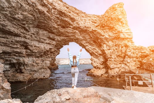 woman sea travel. A woman in a blue jacket stands on a rock above a cliff above the sea, looking at the stormy ocean. Girl traveler rests, thinks, dreams, enjoys nature.