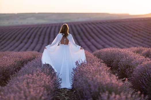 Happy woman in a white dress and straw hat strolling through a lavender field at sunrise, taking in the tranquil atmosphere
