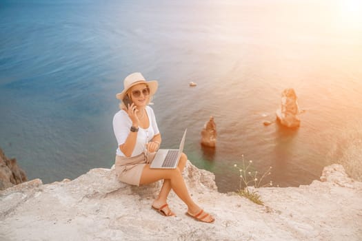 Freelance women sea working on the computer. Good looking middle aged woman typing on a laptop keyboard outdoors with a beautiful sea view. The concept of remote work