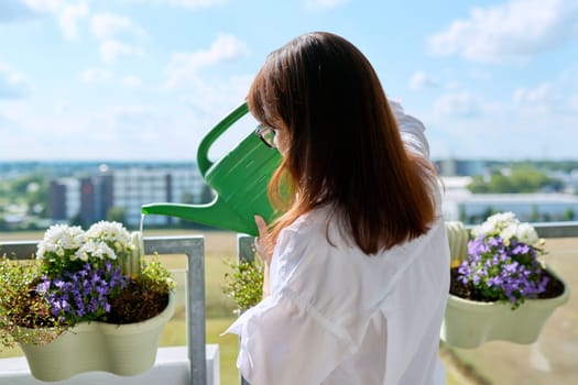 Woman watering potted plants from watering can on outdoor terrace at home. Green hobby, home gardening, eco trends