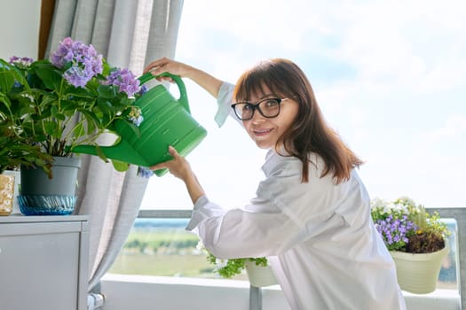 Woman watering potted plants from watering can on outdoor terrace at home. Green hobby, home gardening, eco trends