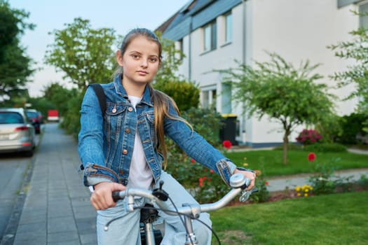 Back to school. Girl child 10, 11 years old with backpack on bicycle on street near house, posing looking at camera. Schoolgirl cycling to school, lifestyle, childhood concept