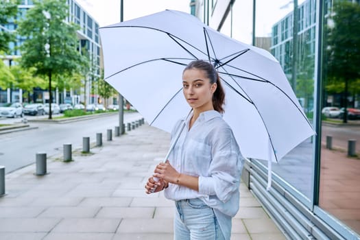 Young teenage female on a summer cloudy day under a white umbrella on a city street