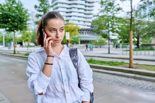 Young attractive teenage girl talking on mobile phone, outdoor on street of modern city. Teenager, college student with backpack, communicating on smartphone. Urban style, lifestyle, youth