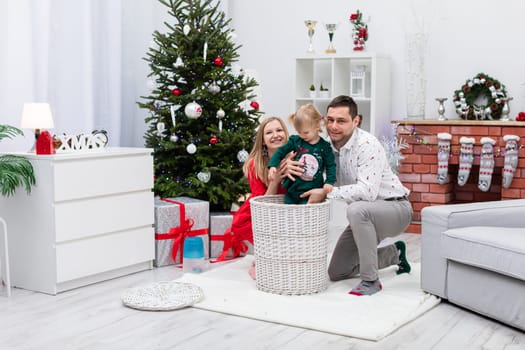 The little girl is dressed in a dark green sweatshirt. The child is standing in a white wicker basket. On either side of the little girl are mom and dad, who are hugging their child and smiling.