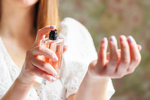 Beautiful young woman using perfume at home.