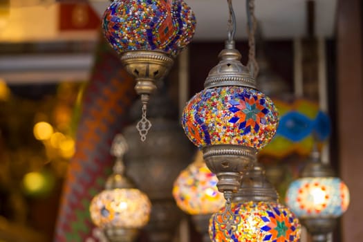 Middle Eastern lambas of different colors and sizes are hanging in the bazaar. Bright traditional Arabic and Turkish lanterns made of metal and glass, inlaid with mosaic details of different colors.