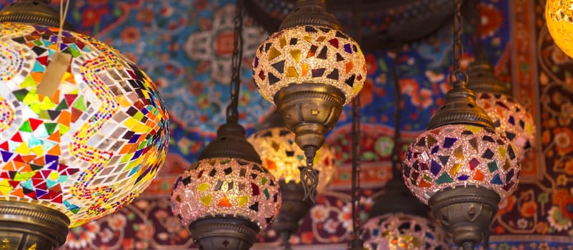Middle Eastern lambas of different colors and sizes are hanging in the bazaar. Bright traditional Arabic and Turkish lanterns made of metal and glass, inlaid with mosaic details of different colors.