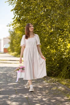 Beautiful girl with flowers, in a dress, glasses and sneakers. A beautiful bouquet of flowers in a box in the hands of a beautiful girl who walks along the street on a sunny day.