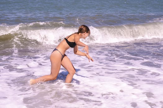 A girl in swimsuit runs along the sea. Attractive teenage girl in a bikini runs along the seashore with her arms outstretched