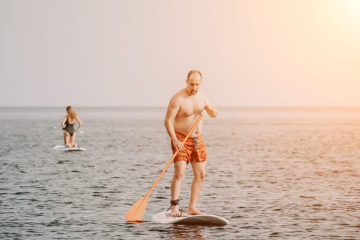 Active mature male paddler with his paddleboard and paddle on a sea at summer. Happy senior man stands with a SUP board. Stand up paddle boarding - outdor active recreation in nature