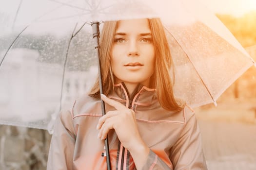 Woman rain park. Happy woman portrait wearing a raincoat with transparent umbrella outdoors on rainy day in park near sea. Girl on the nature on rainy overcast day