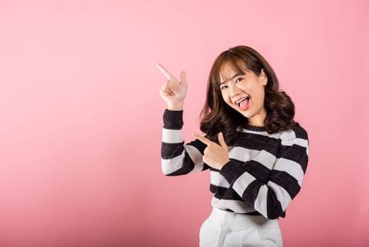 Smiling happy woman pointing finger out space, Portrait Asian beautiful young female point into empty looking to side away, studio shot isolated on pink background with copy space