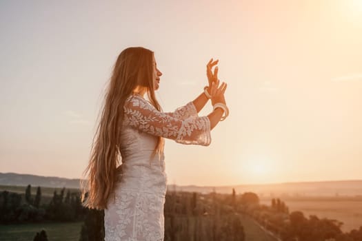 Romantic beautiful bride in white dress posing with sea and mountains in background. Stylish bride standing back on beautiful landscape of sea and mountains on sunset