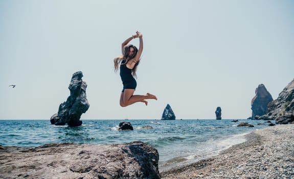 Woman travel sea. Young Happy woman in a long red dress posing on a beach near the sea on background of volcanic rocks, like in Iceland, sharing travel adventure journey