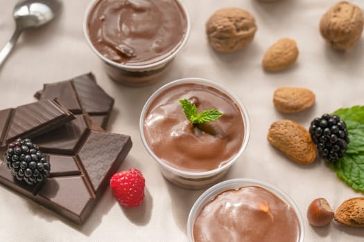 three Chocolate Trifle in cups with pieces of chocolate, strawberries, hazelnuts