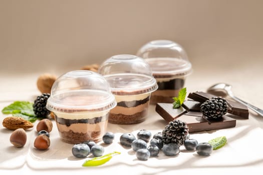 three Chocolate Trifle in cups with pieces of chocolate, strawberries, hazelnuts