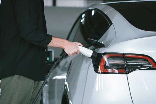 Young man travel with EV electric car to shopping center parking lot charging in downtown city showing urban sustainability lifestyle by green clean rechargeable energy of electric vehicle innards